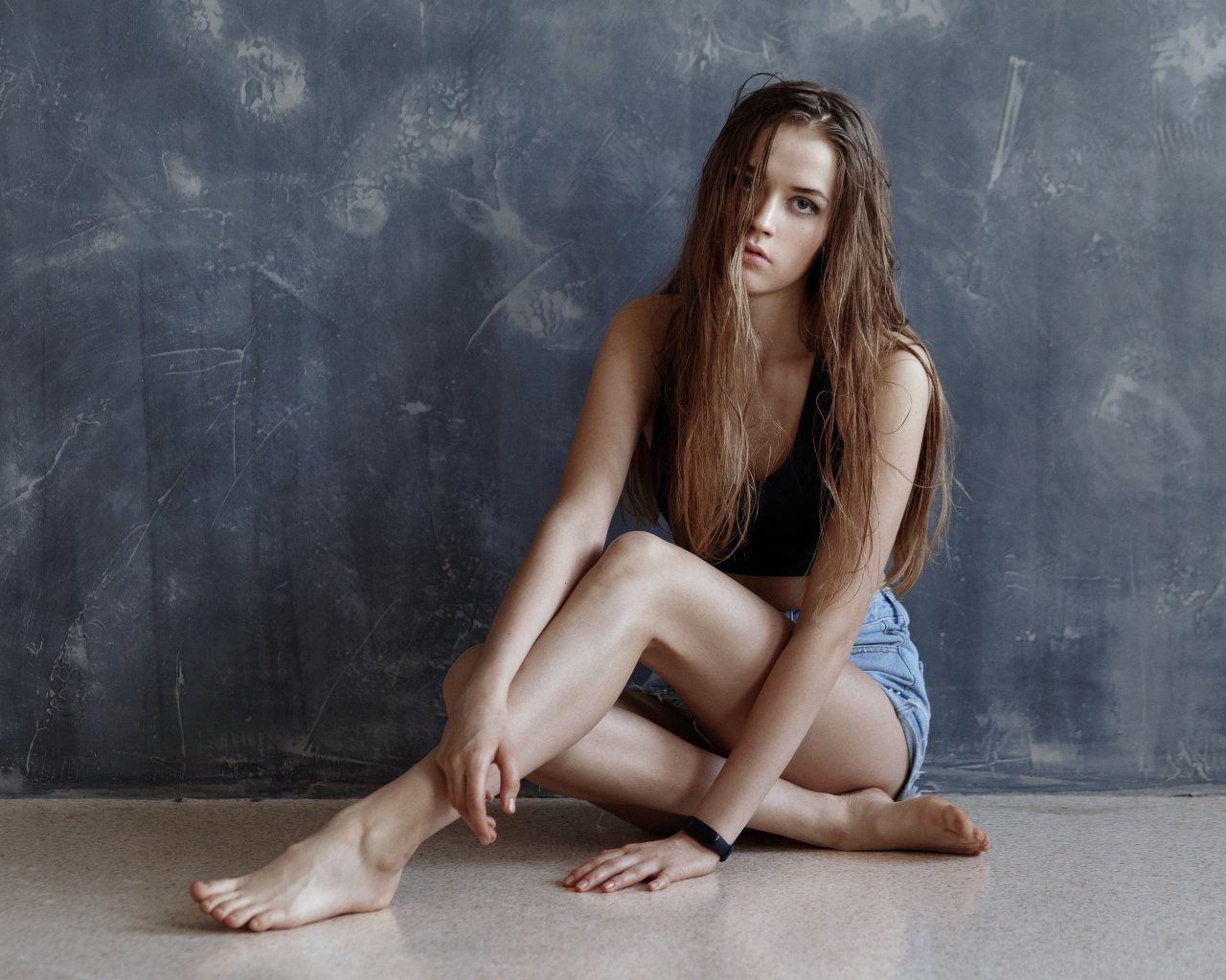 Молодая девушка с мокрыми волосами сидит у стены 