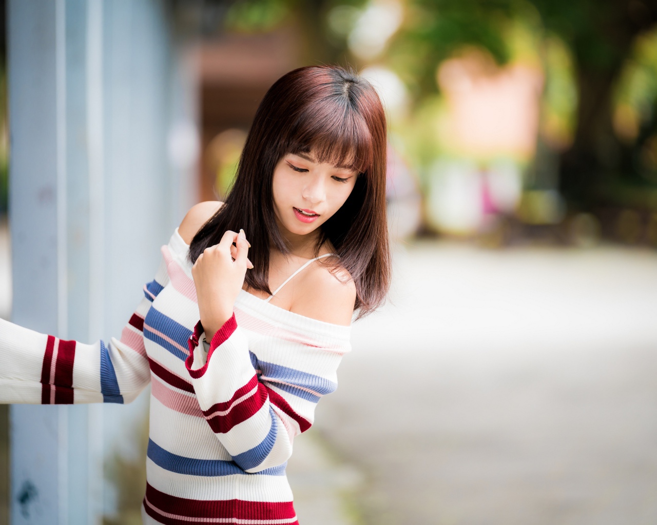 Молодая нежная девушка азиатка в свитере стоит у забора 