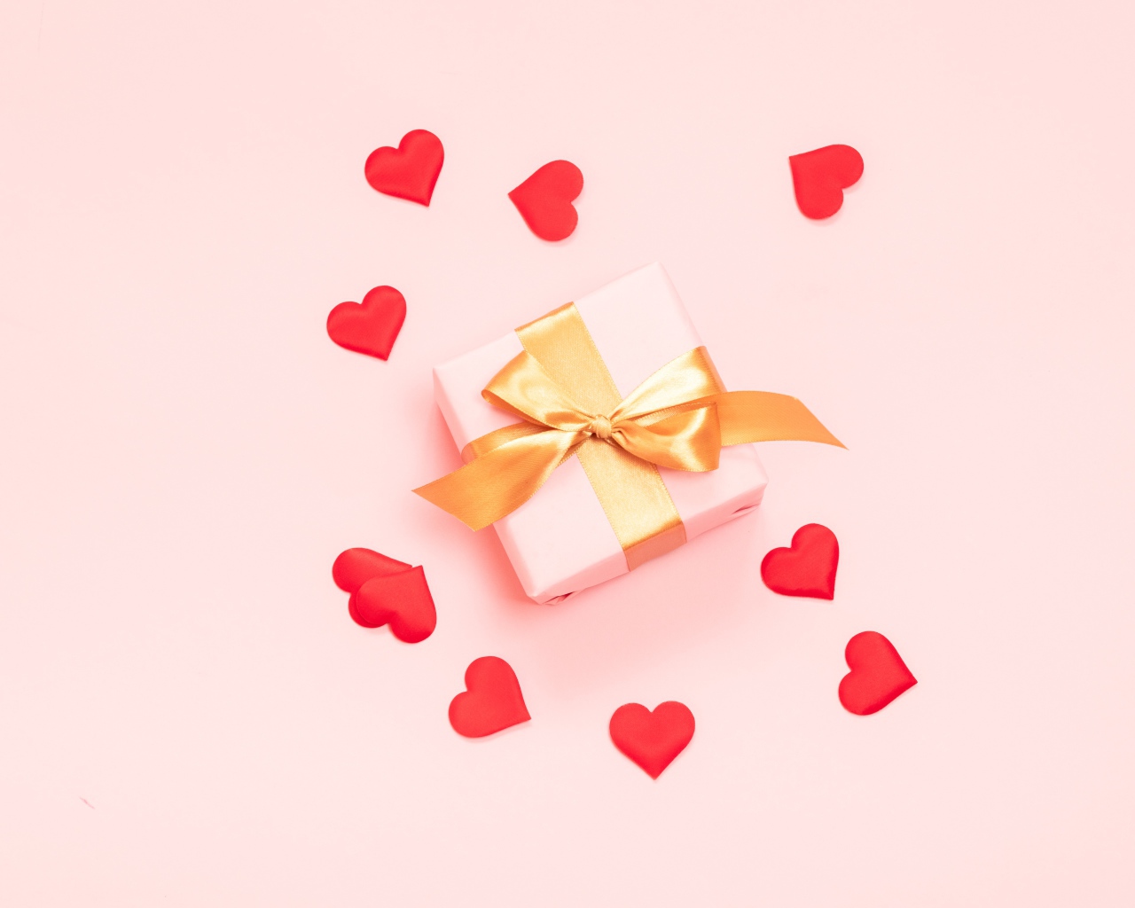 Gift with bow on a pink background with red hearts.