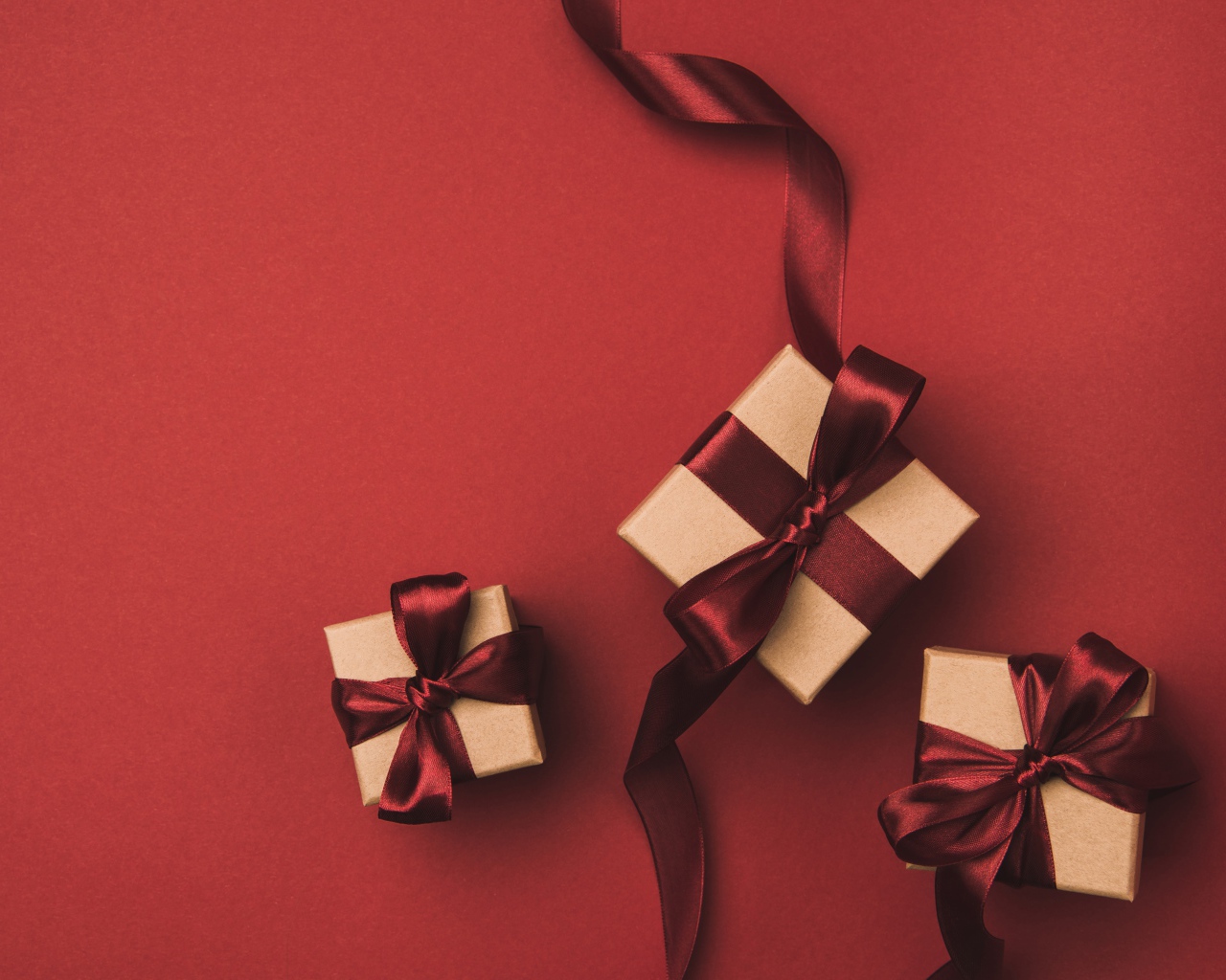 Три подарочные коробки с бантами на красном фоне