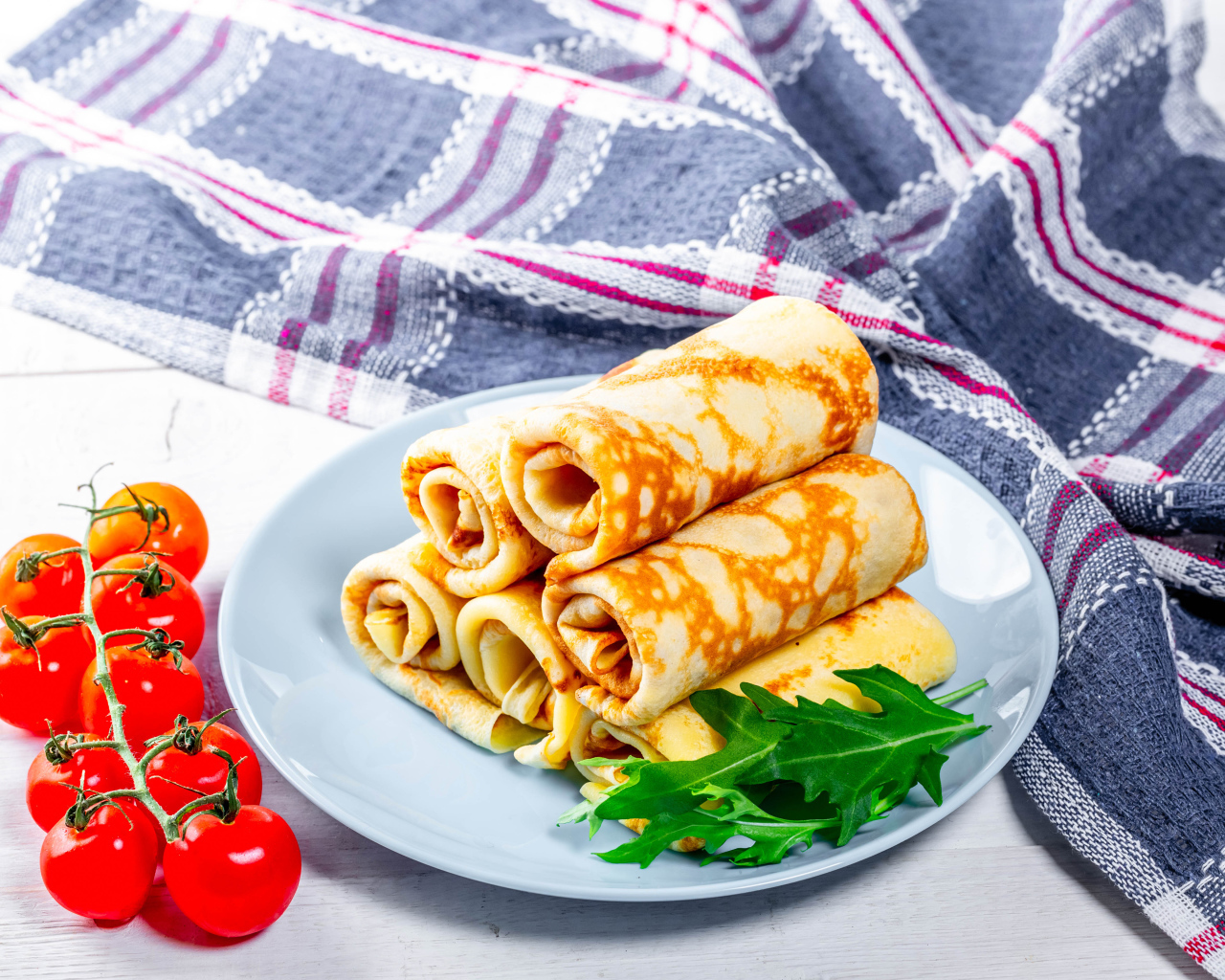 Блинчики на столе с помидорами и полотенцем угощение на Масленицу 2020