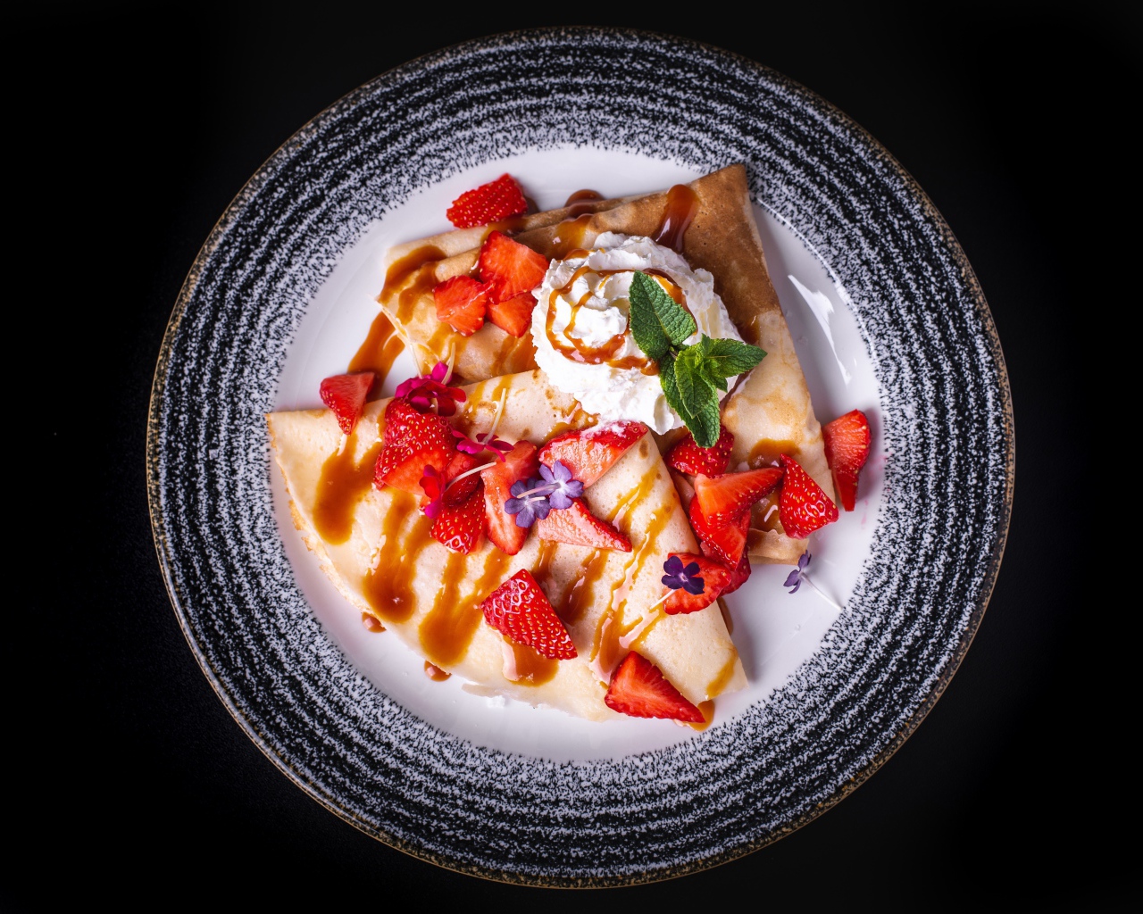 Тонкие блинчики со сливками на тарелке с клубникой и сиропом вид сверху