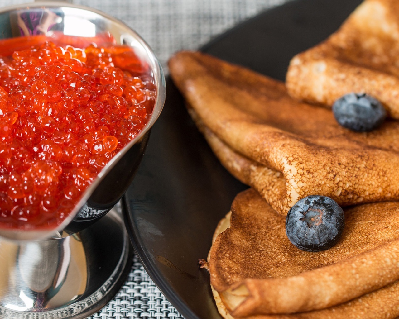 Тонкие блины с ягодами черники на столе с красной икрой на Масленицу