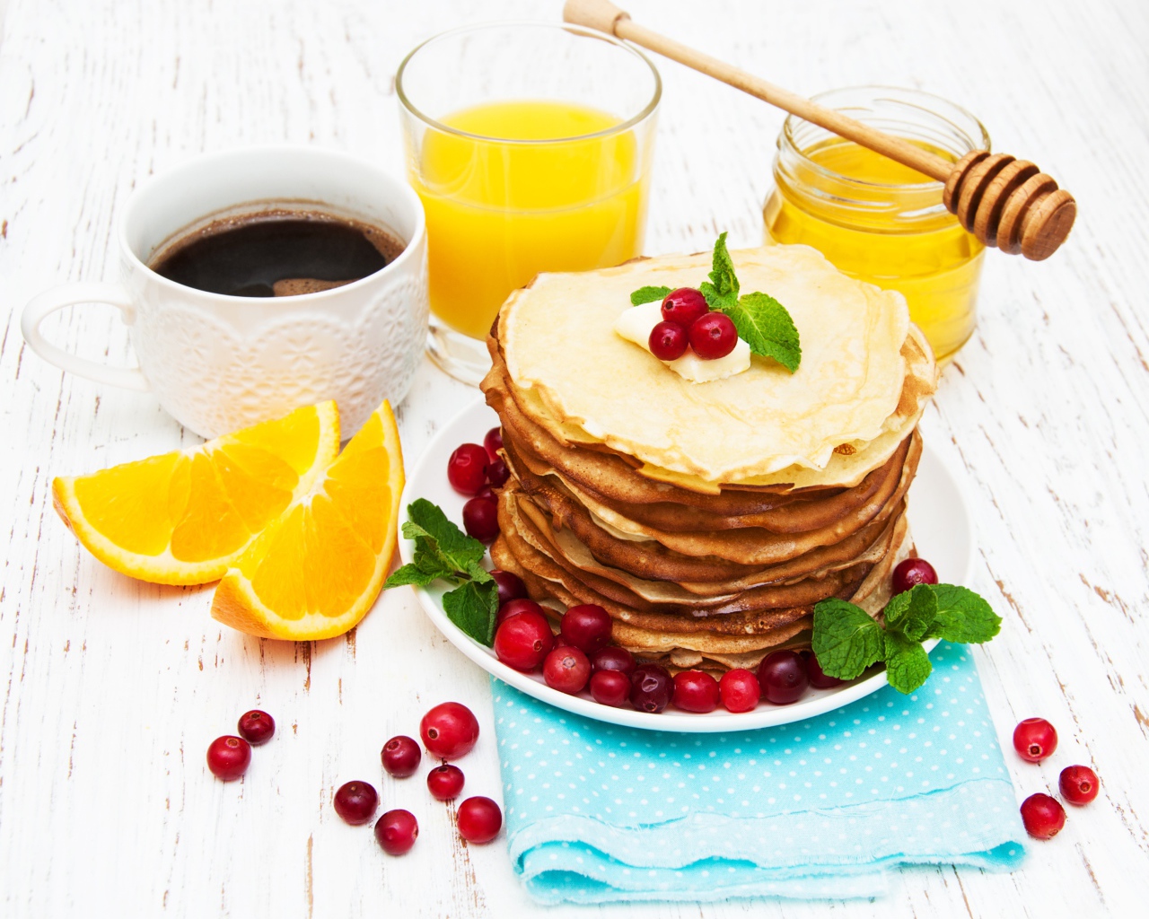 Тонкие румяные блинчики на столе с ягодами клюквы, апельсинами, медом и кофе