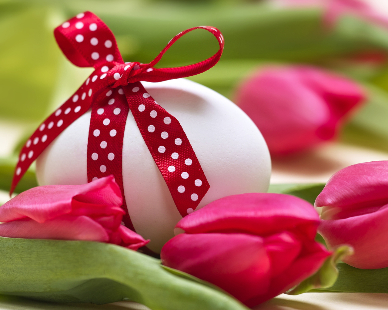 Яйцо с бантом на столе с тюльпанами на праздник Пасха