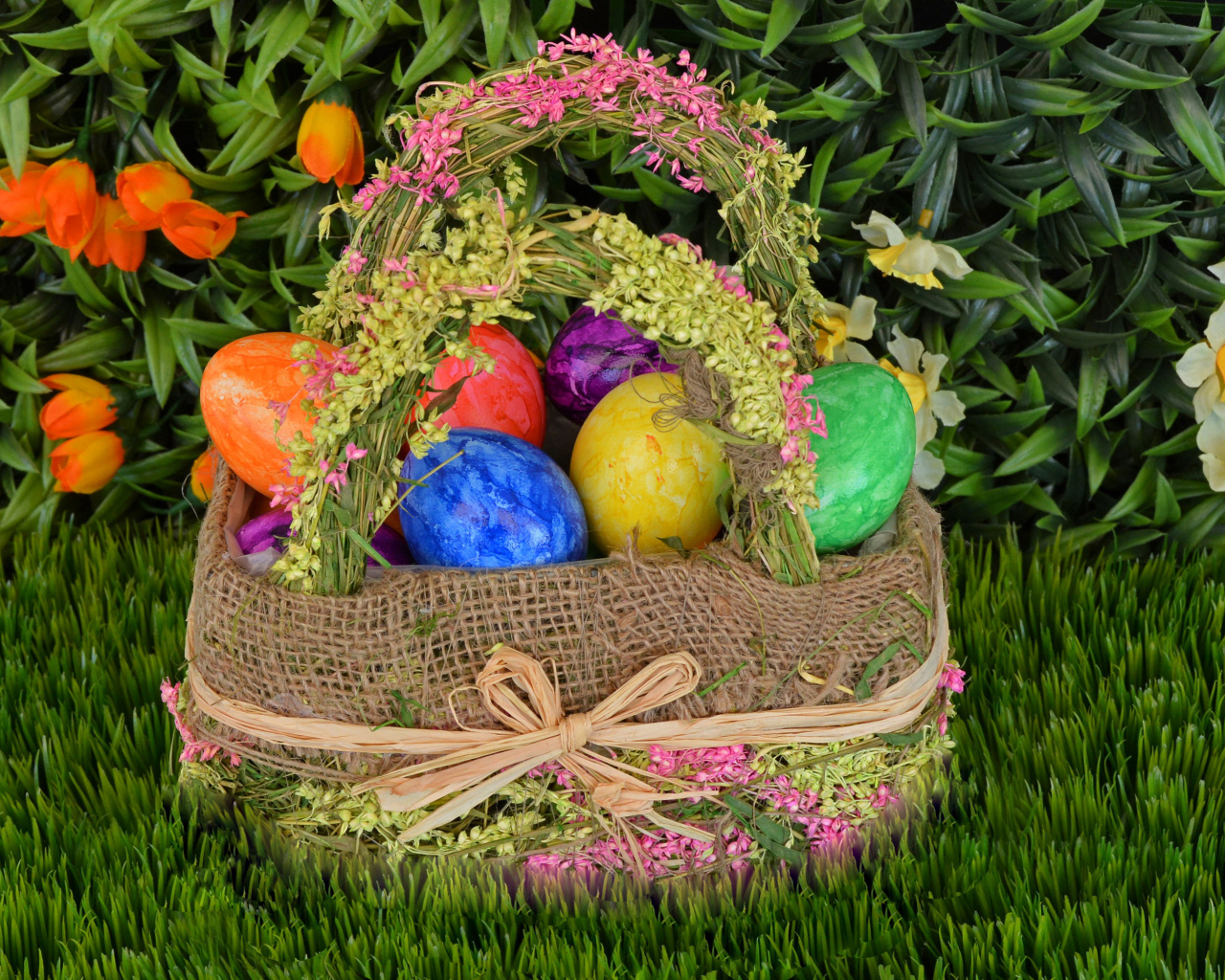 Разноцветные пасхальные яйца в корзине на зеленой траве на праздник 