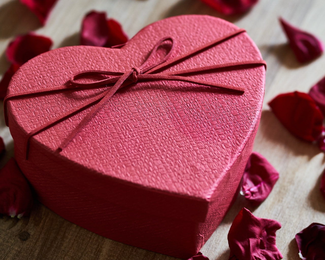 Большая красная коробка в форме сердца на столе с лепестками роз