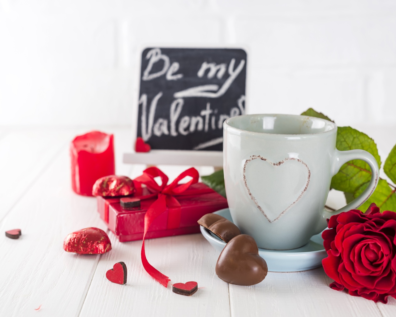 Белая чашка с конфетами и красной розой на столе в подарок на 14 февраля