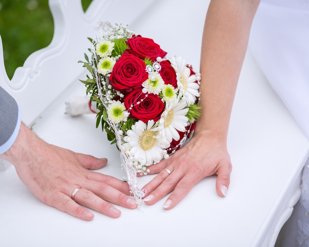 Two hands with wedding rings and bridal bouquet