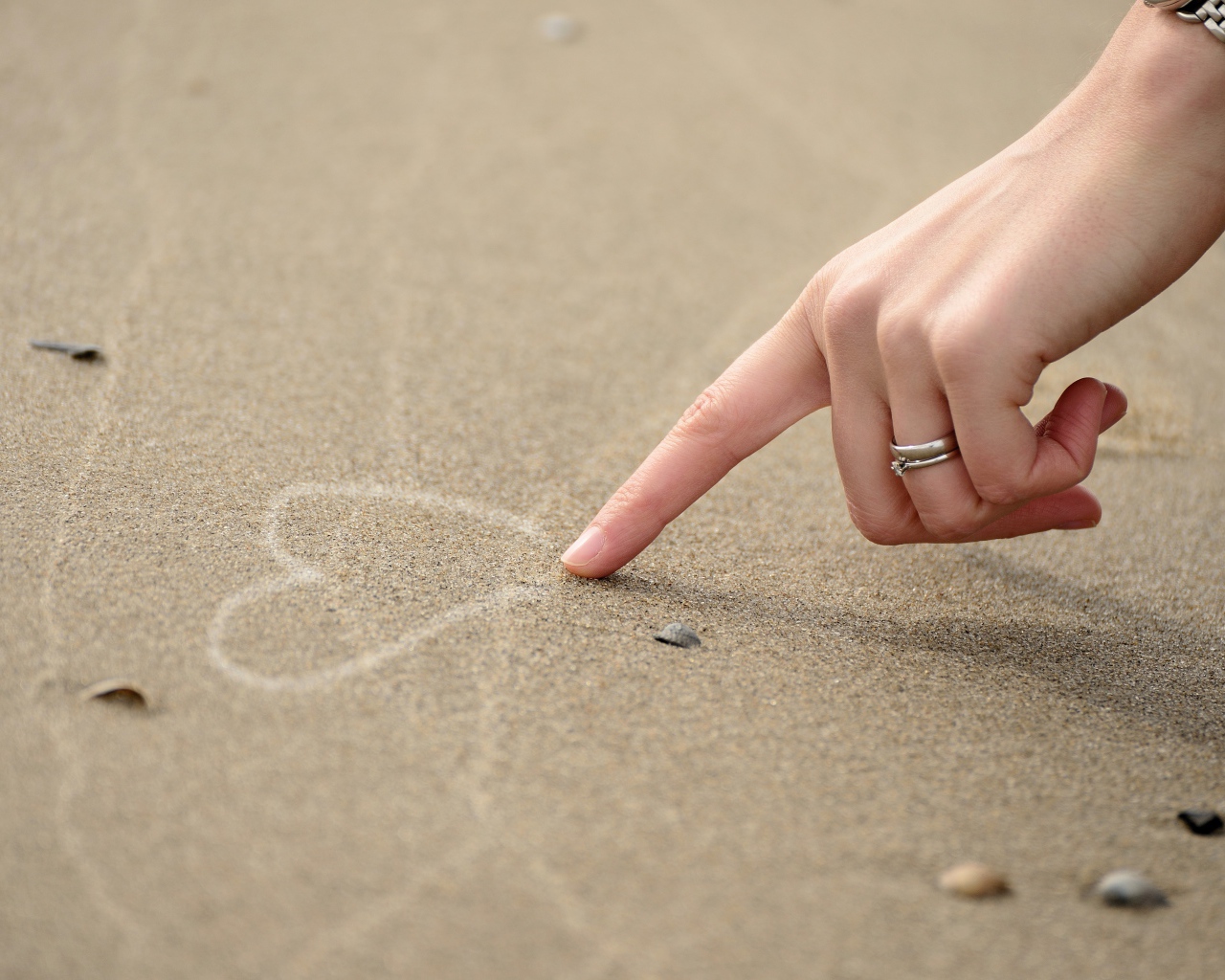 Девушка рисует сердце на песке 