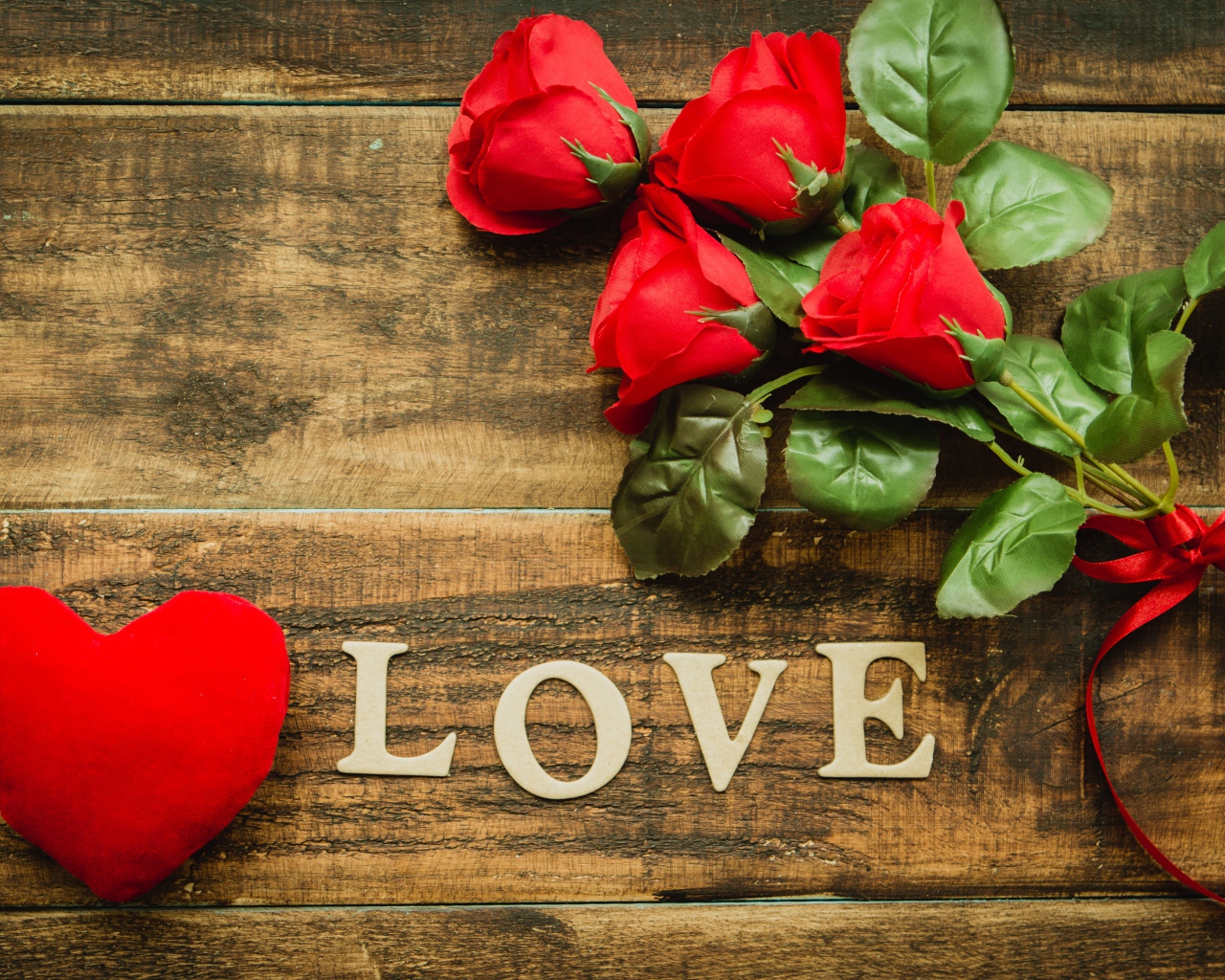 Надпись LOVE на столе с розами и красным сердцем