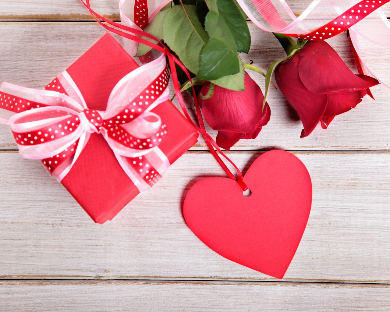 Красные розы с подарком и красным сердцем на деревянном столе