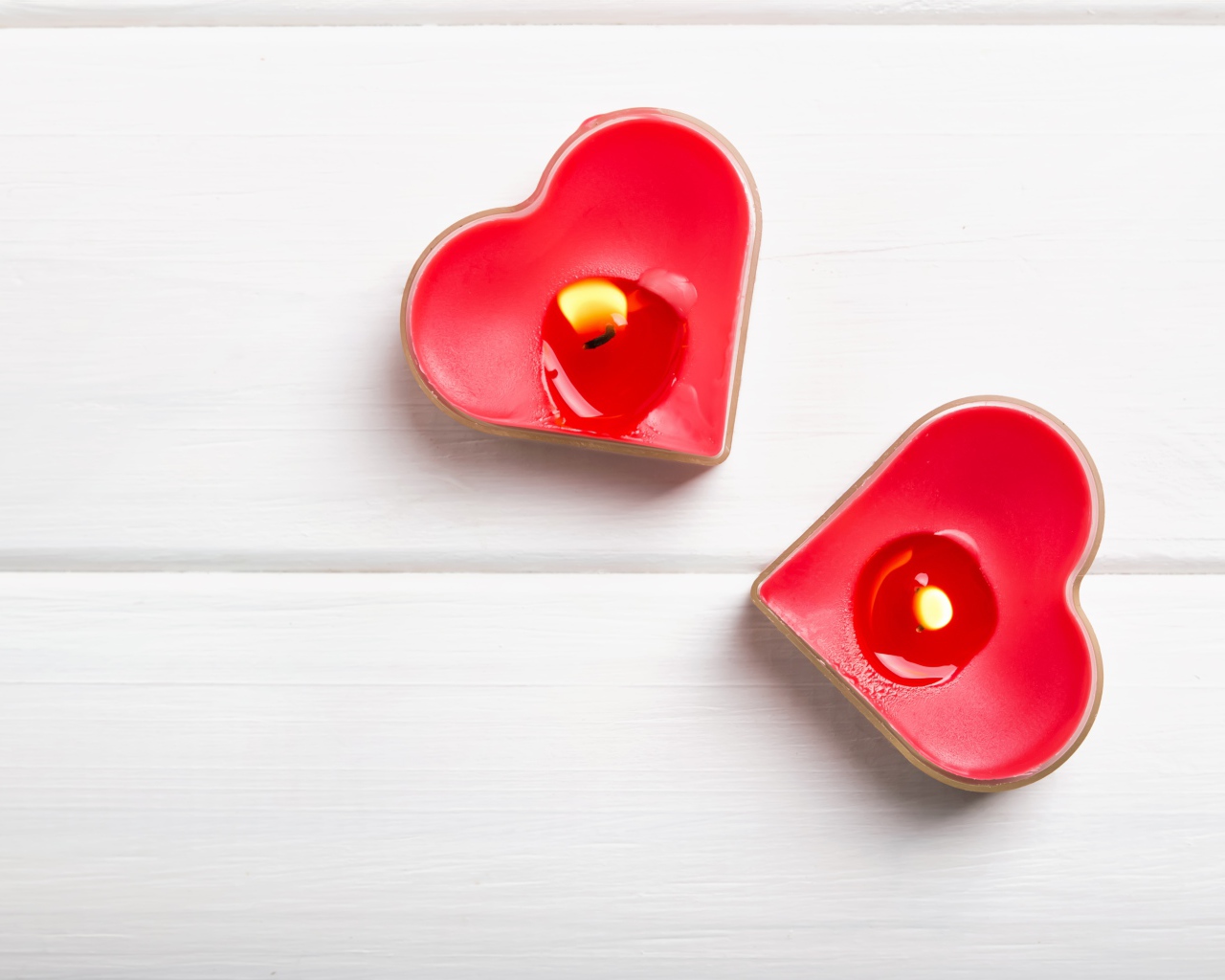 Две зажженные свечи в форме сердца на столе 