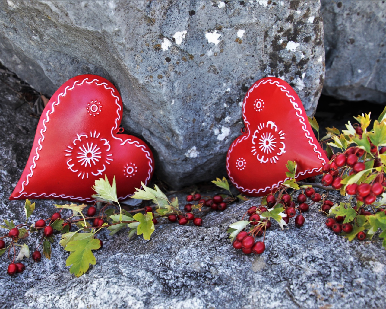Два сердца лежат у камня с красными ягодами