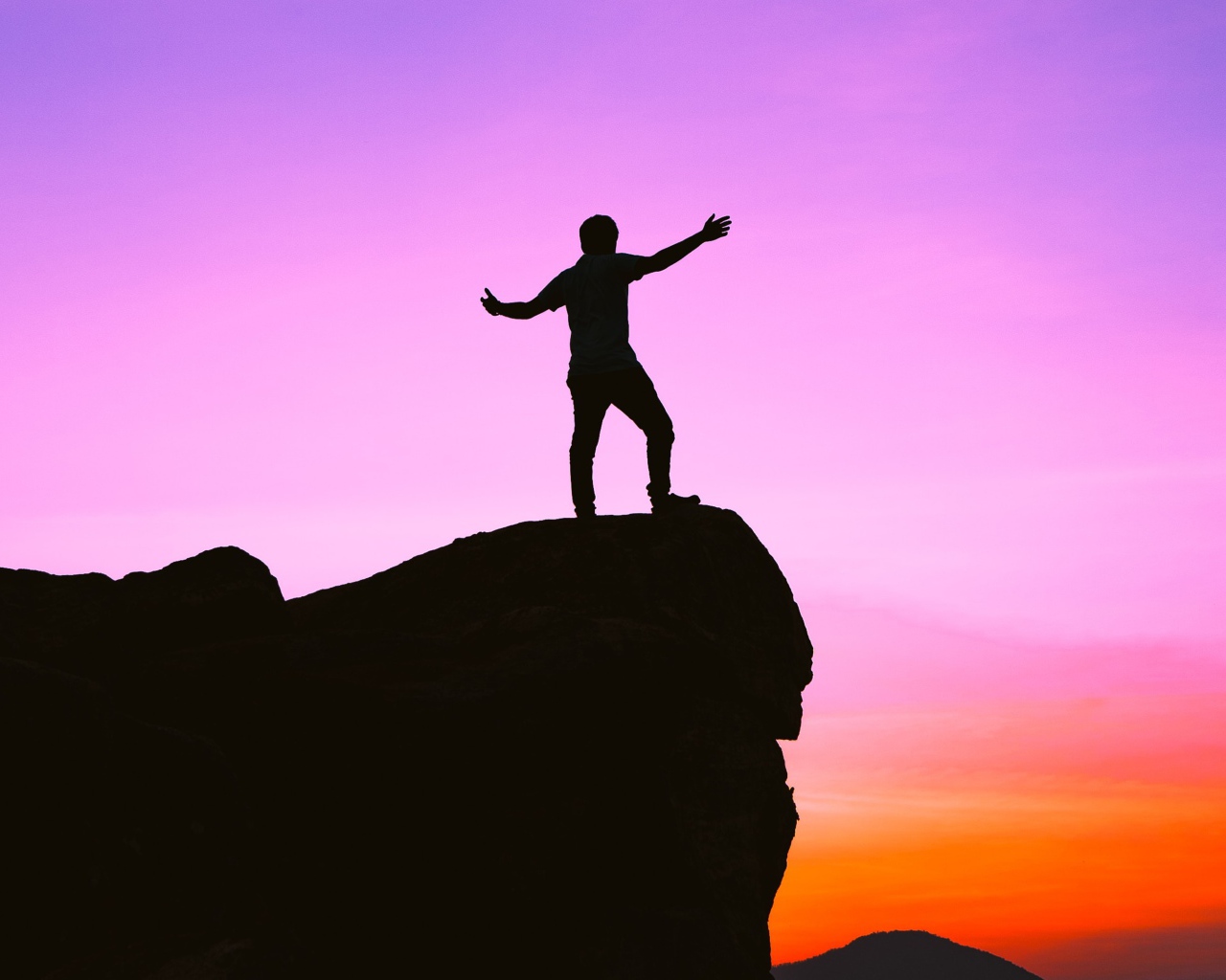 Мужчина стоит на краю утеса на закате