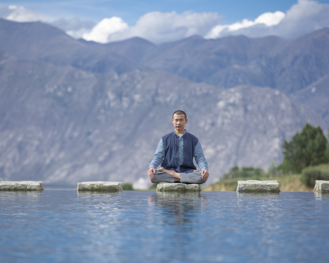 Мужчина азиат в позе лотоса медитирует у воды 