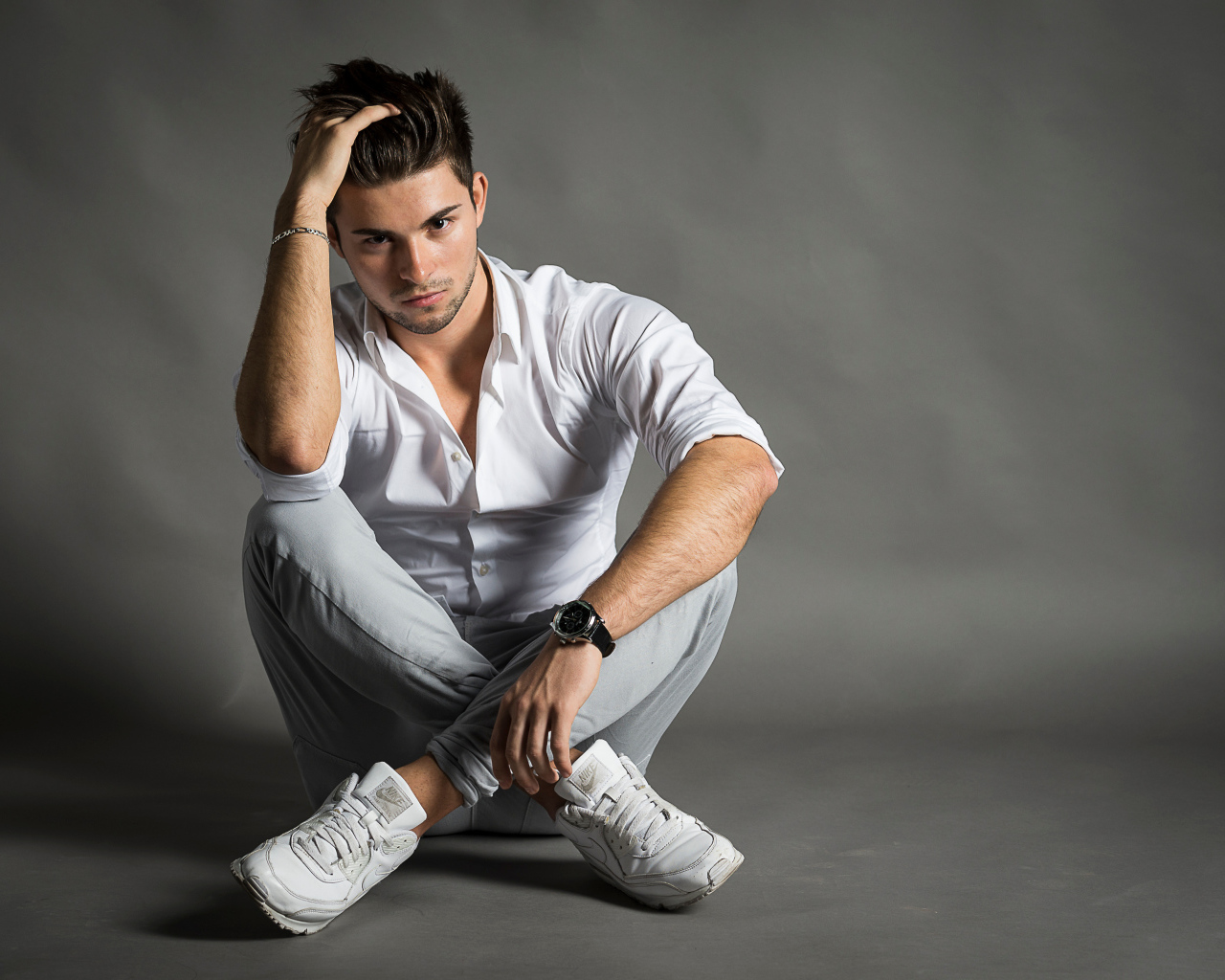 Красивый молодой человек в белой рубашке сидит у стены 