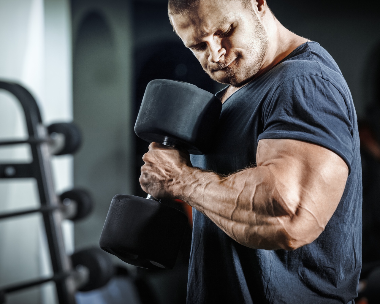 Мужчина бодибилдер в спортзале с гантелей 