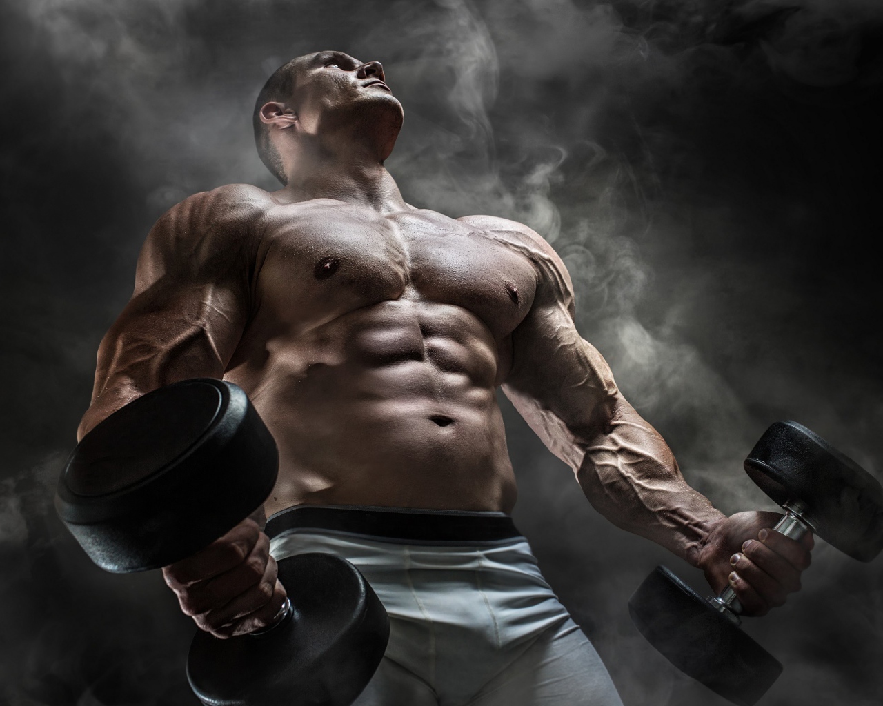 Мужчина бодибилдер с тяжелыми гантелями в руках