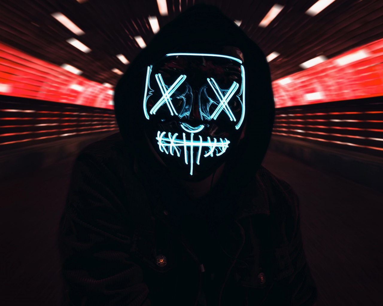 Парень в черной куртке в неоновой маске анонимуса на лице