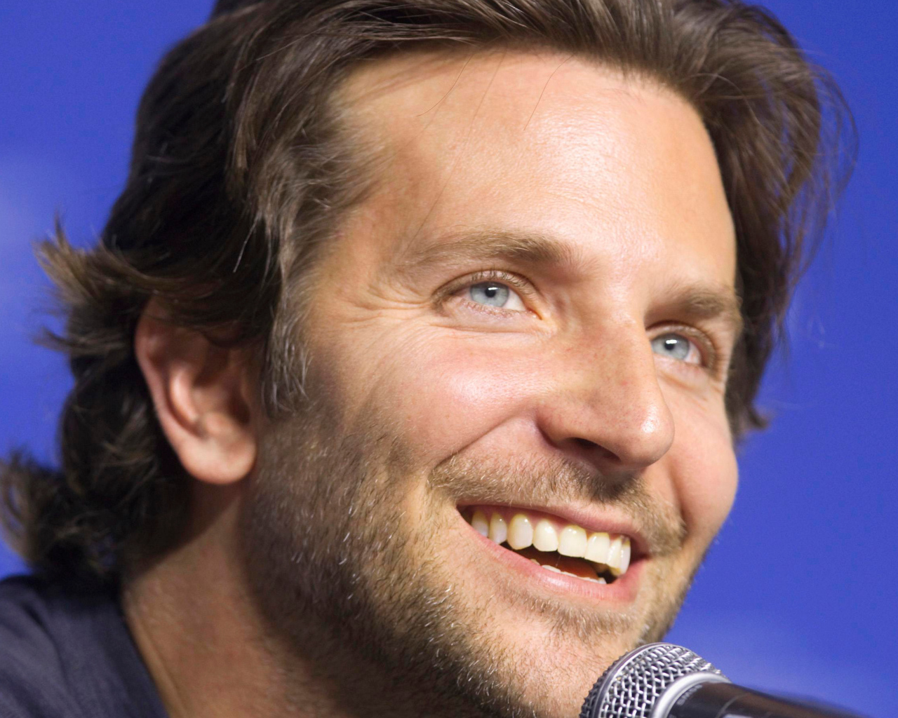 Голубоглазый актер Брэдли Купер с микрофоном на синем фоне