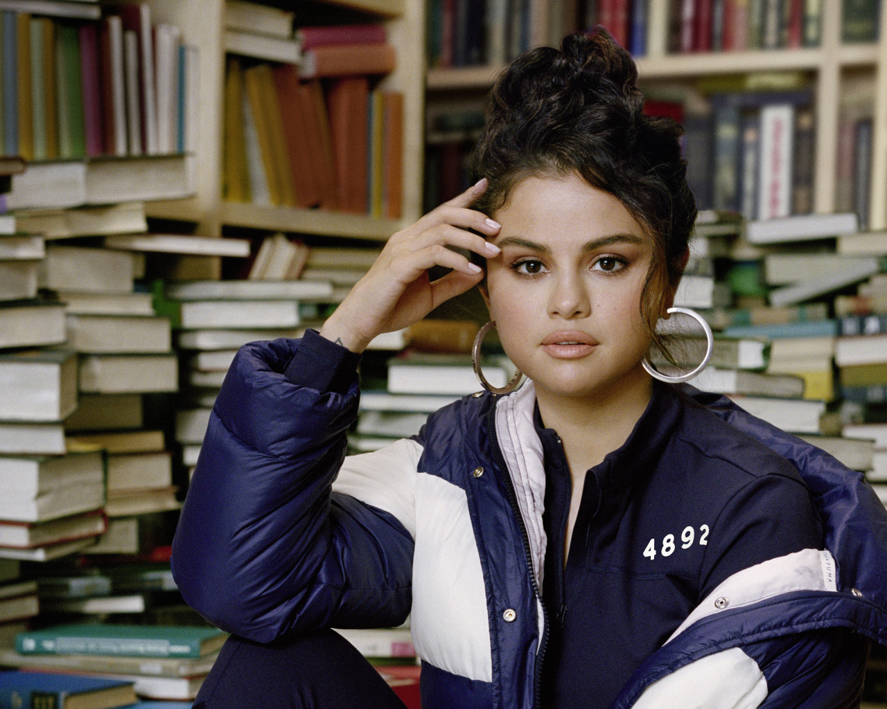 Actress and singer Selena Gomez in a jacket sits in a library