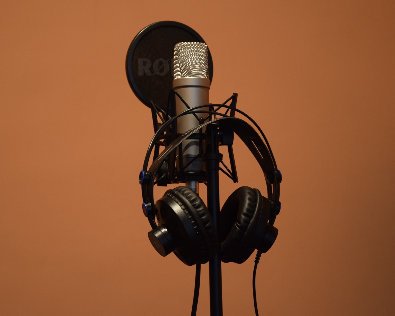 Condenser microphone with headphones on brown background