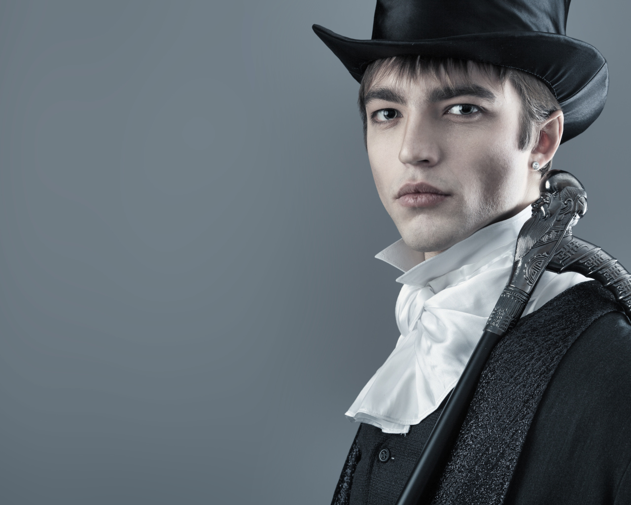 Красивый молодой человек в черном цилиндре и фраке на сером фоне