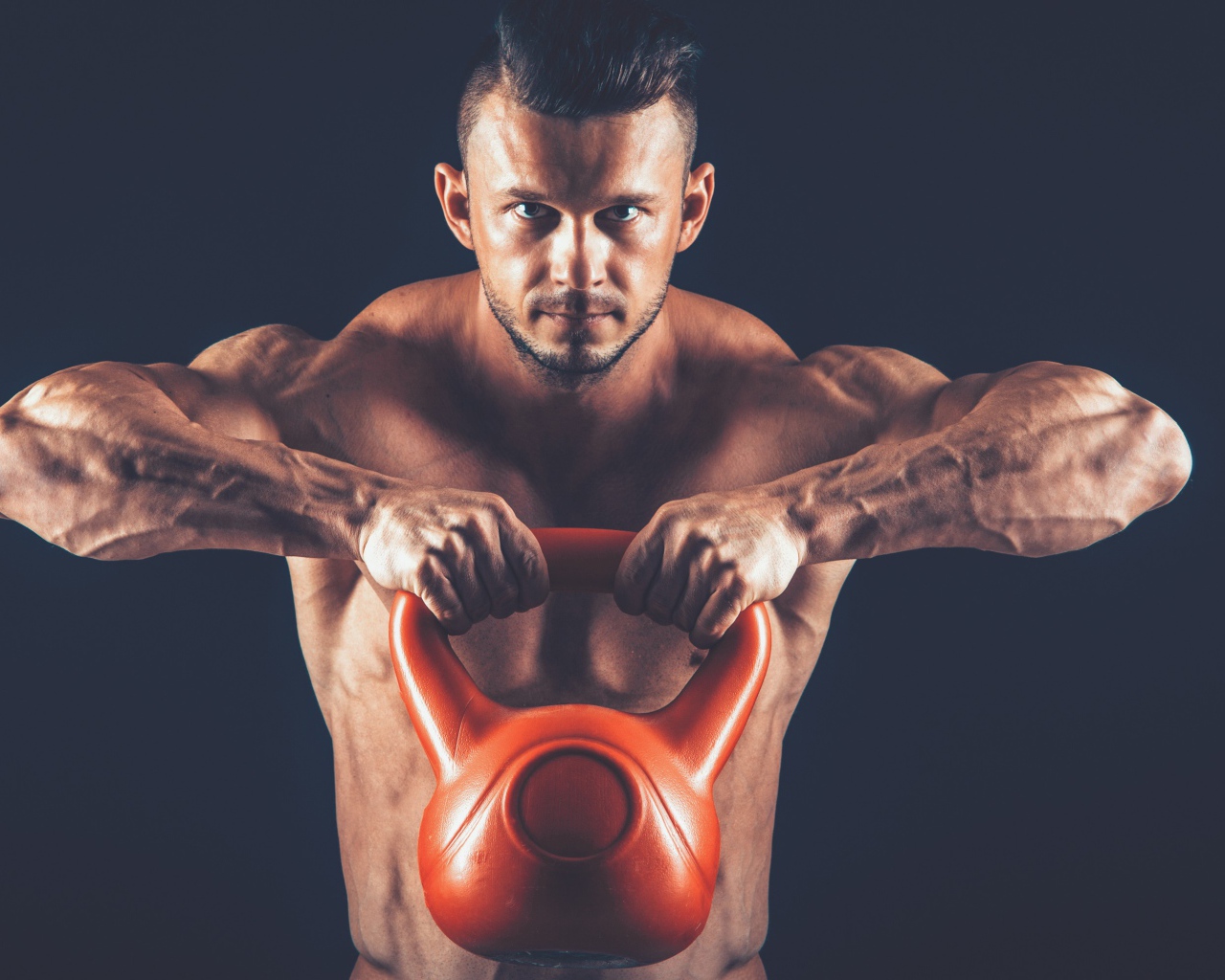 Накаченный парень поднимает тяжелую гирю на черном фоне