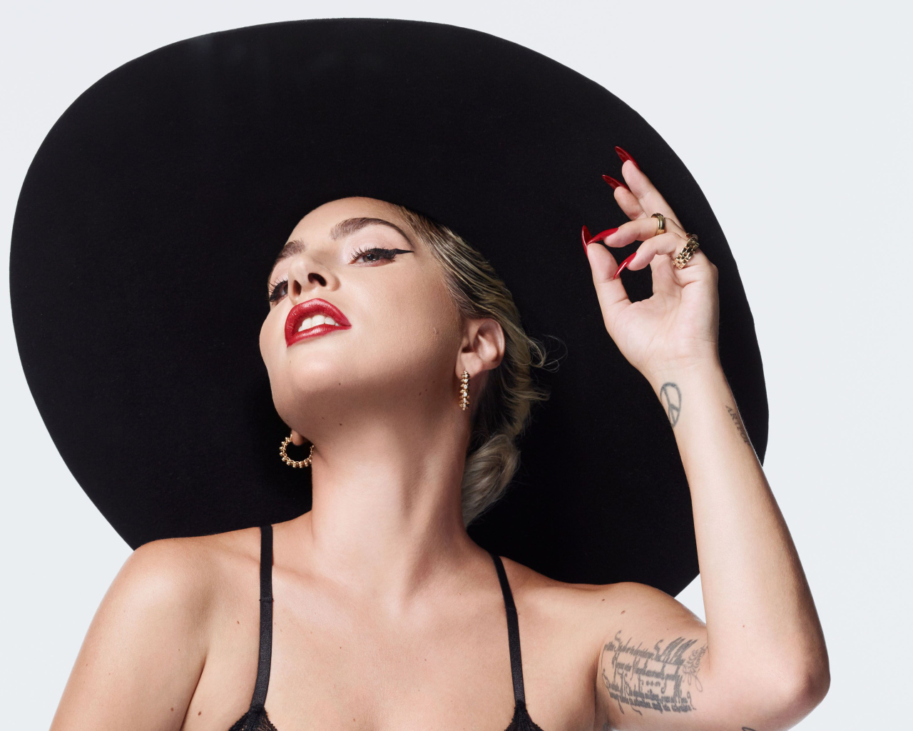 Певица Леди Гага в большой черной шляпе на белом фоне