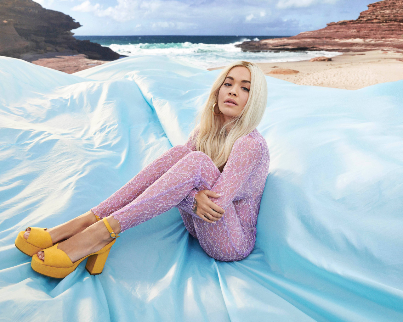 Певица Рита Ора сидит на голубом покрывале у моря