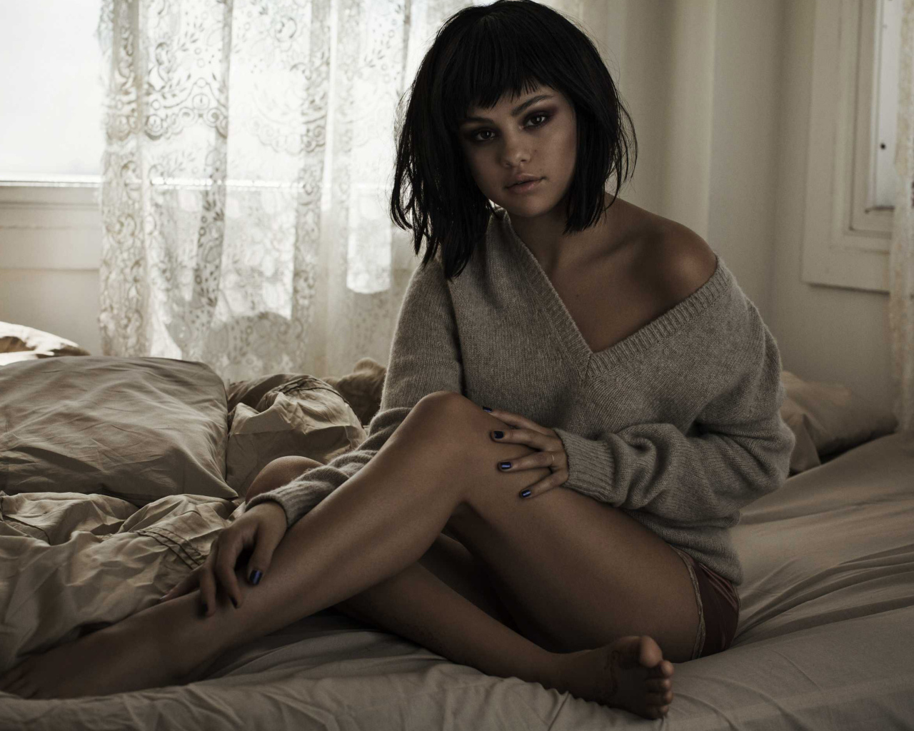 Певица Селена Гомес сидит в свитере на кровати