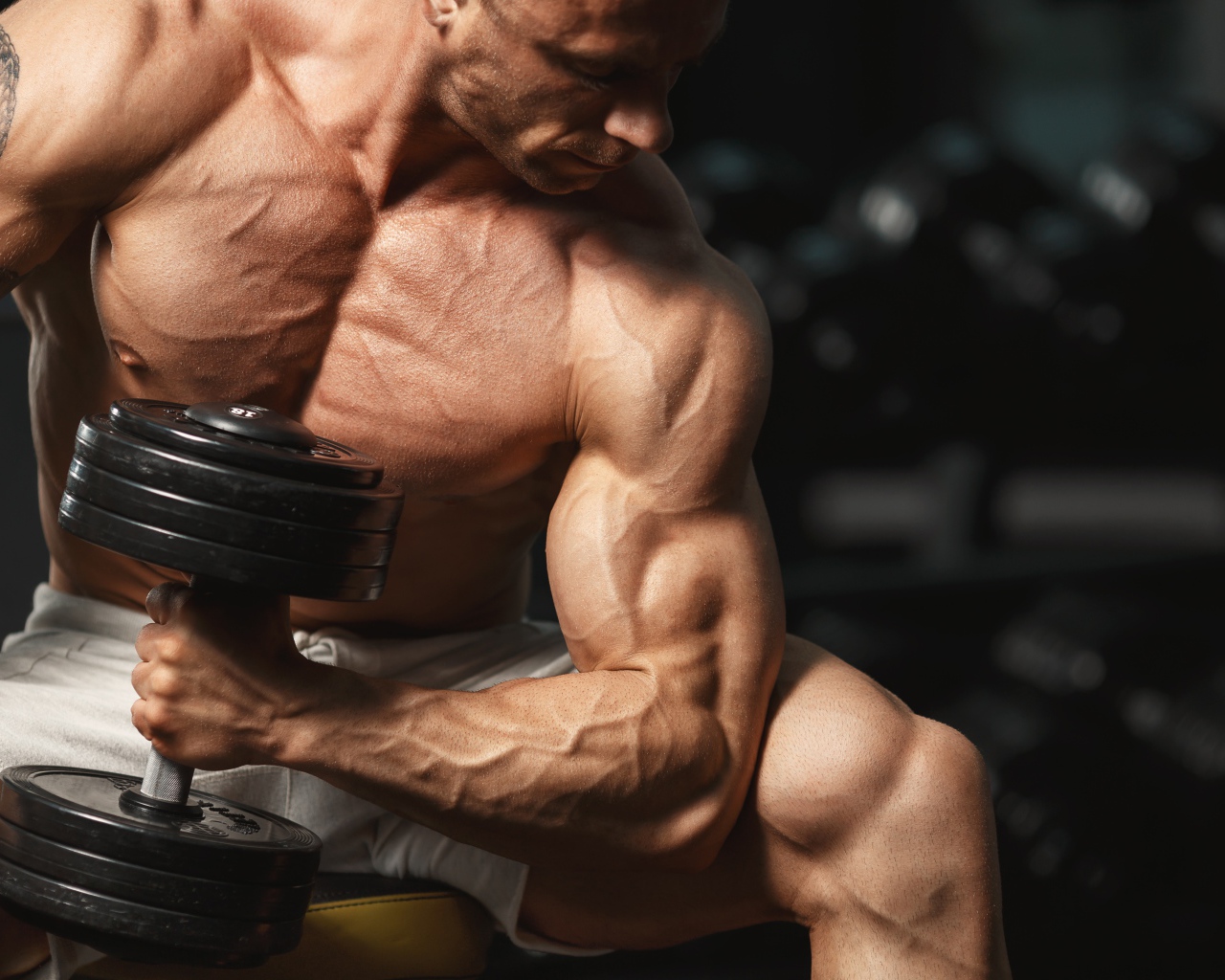 Сильный мужчина качает мускулы гантелей 