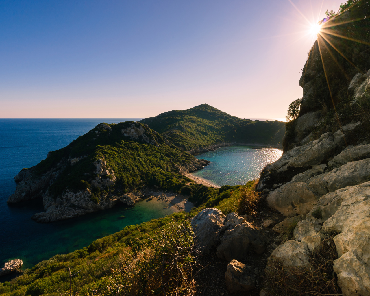 Яркое солнце за скалой у тихого моря