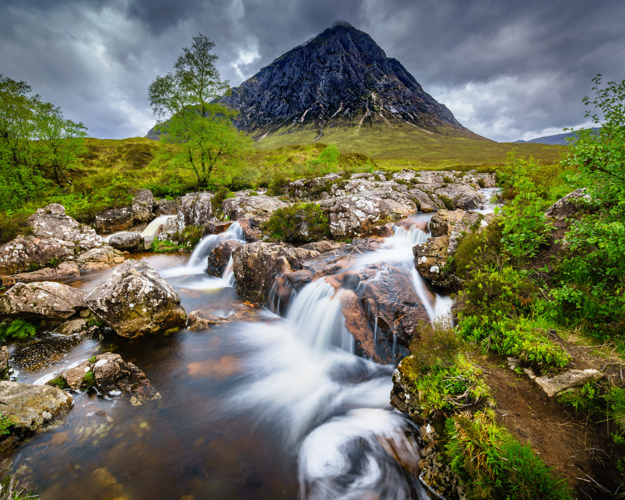 Быстрая вода в реке на фоне высокой горы под грозовым небом 