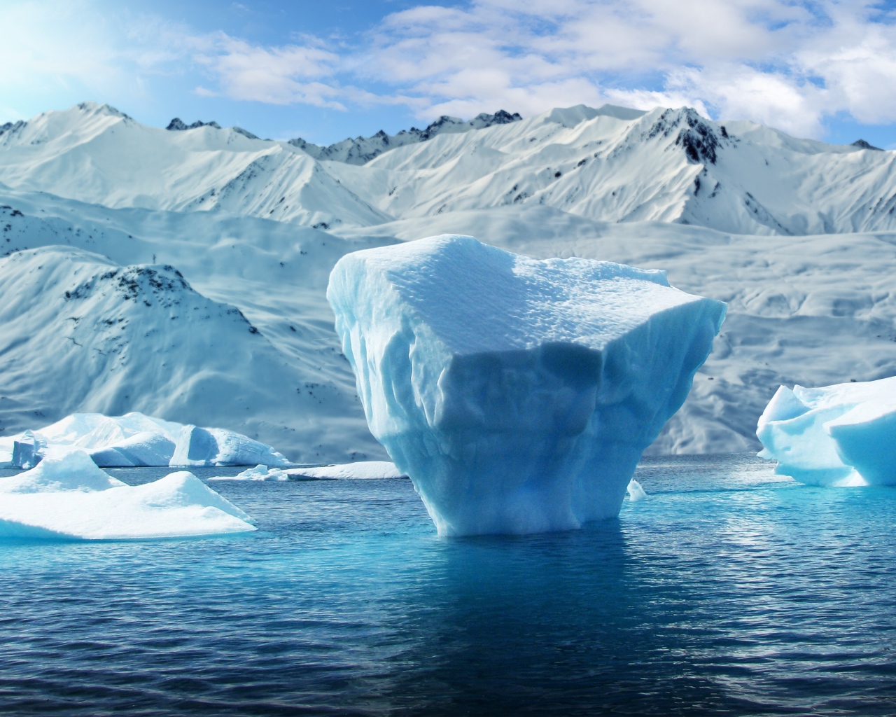 Большие глыбы льда в воде на фоне заснеженных гор 