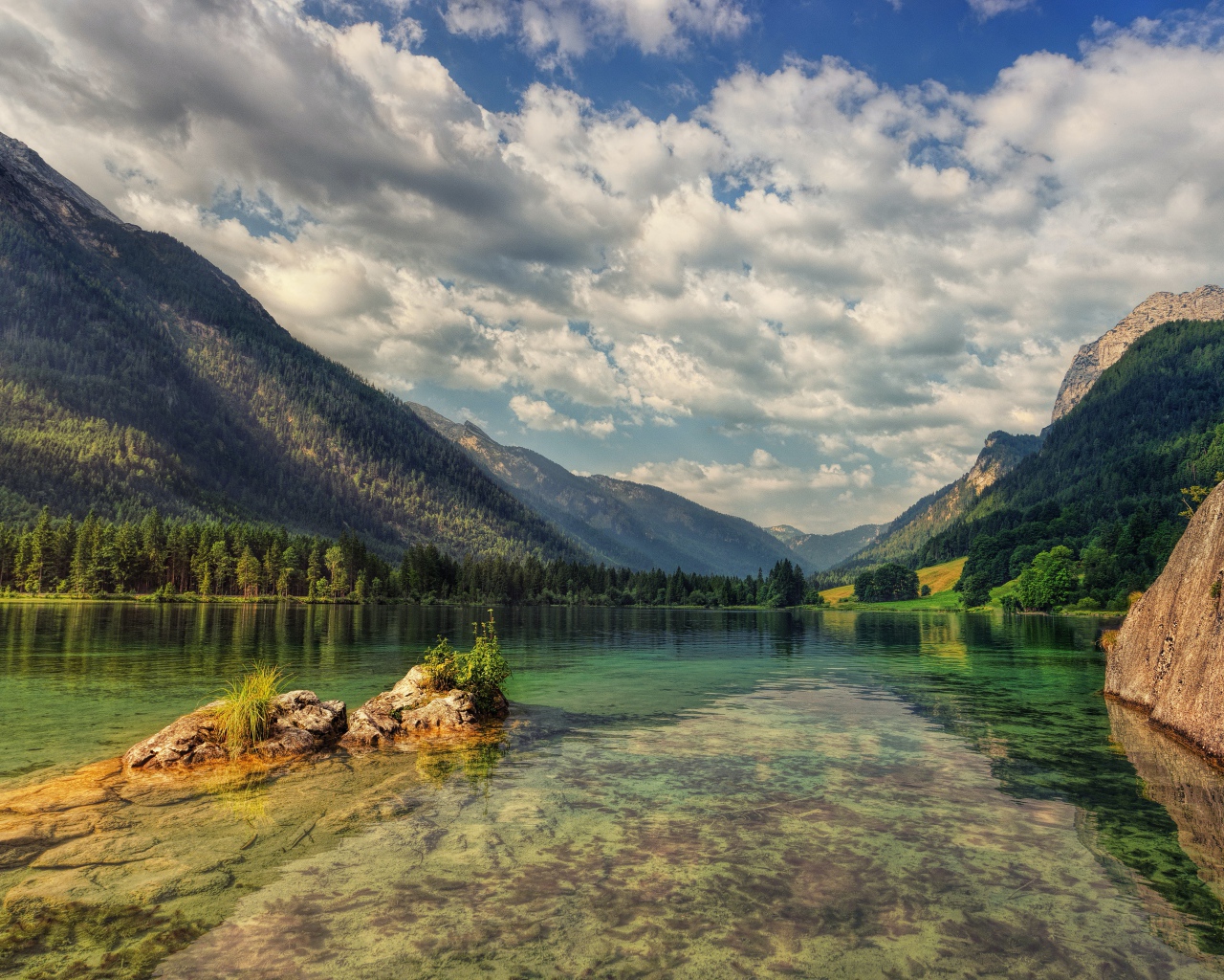 Большие камни в озере на фоне гор под небом с белыми облаками