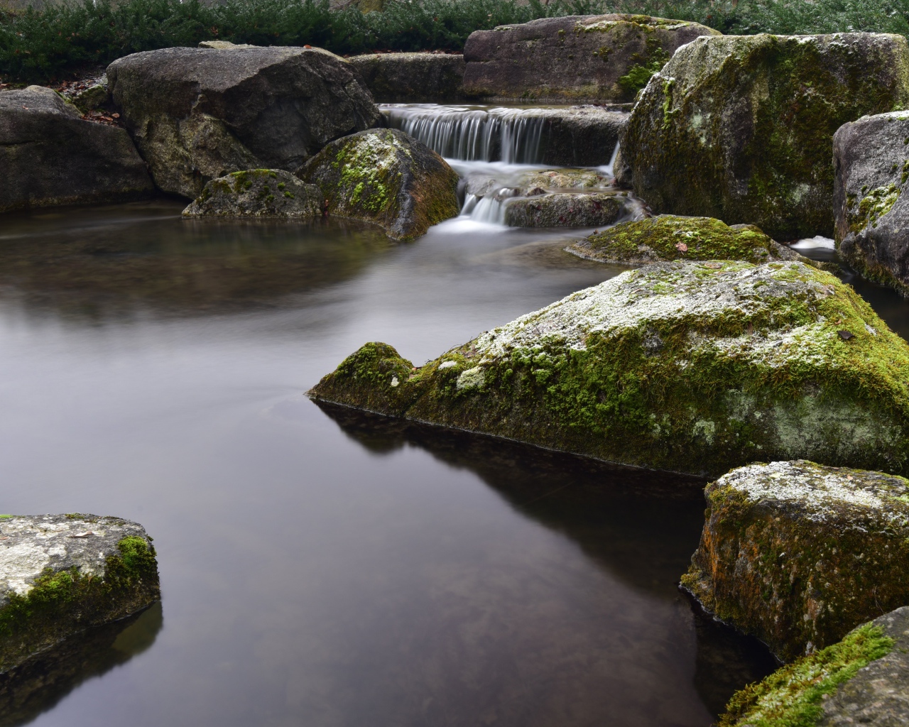 Вода стекает по камням в пруд с большими покрытыми мхом камнями