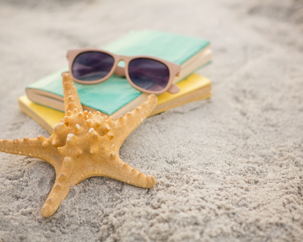 Книги, очки и морская звезда на белом песке 