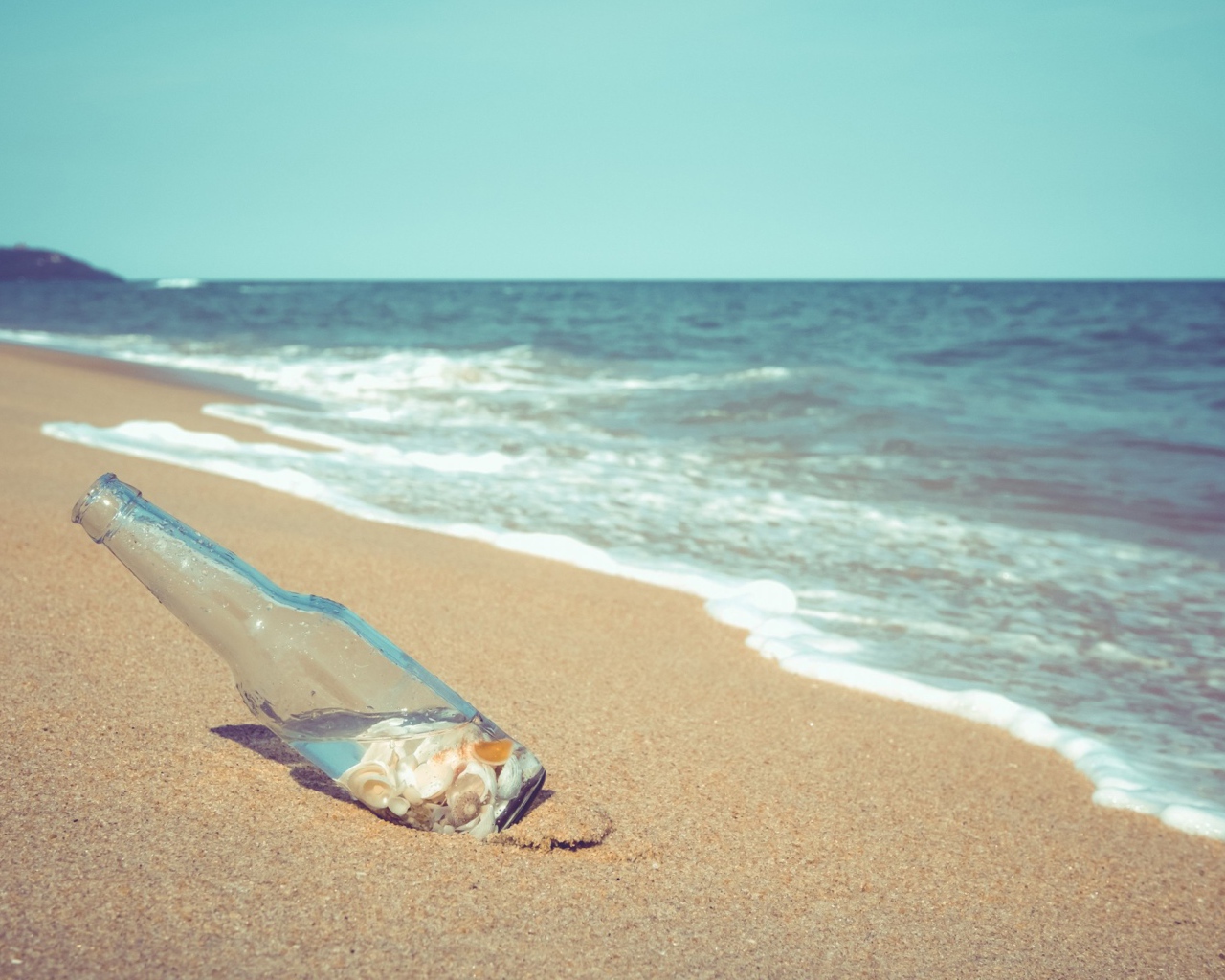 Бутылка с ракушками на песке у моря