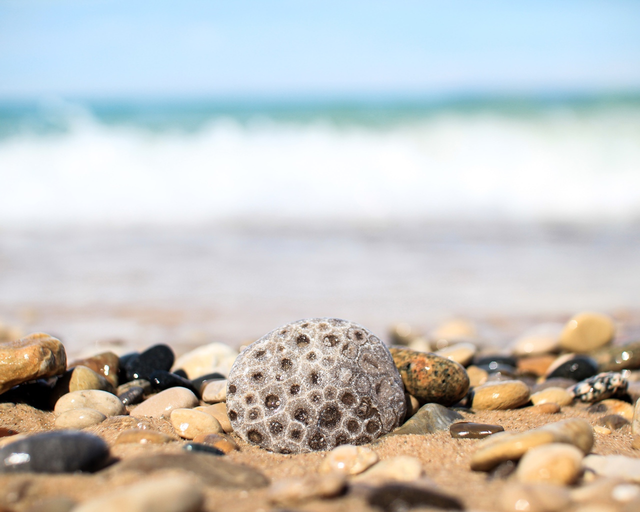 Разные камни лежат на желтом песке у моря 