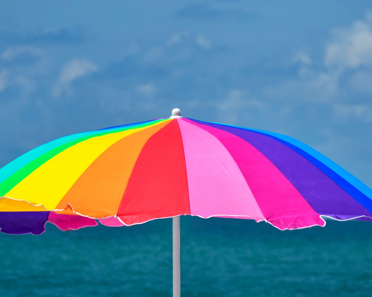 Большой разноцветный пляжный зонт на фоне моря