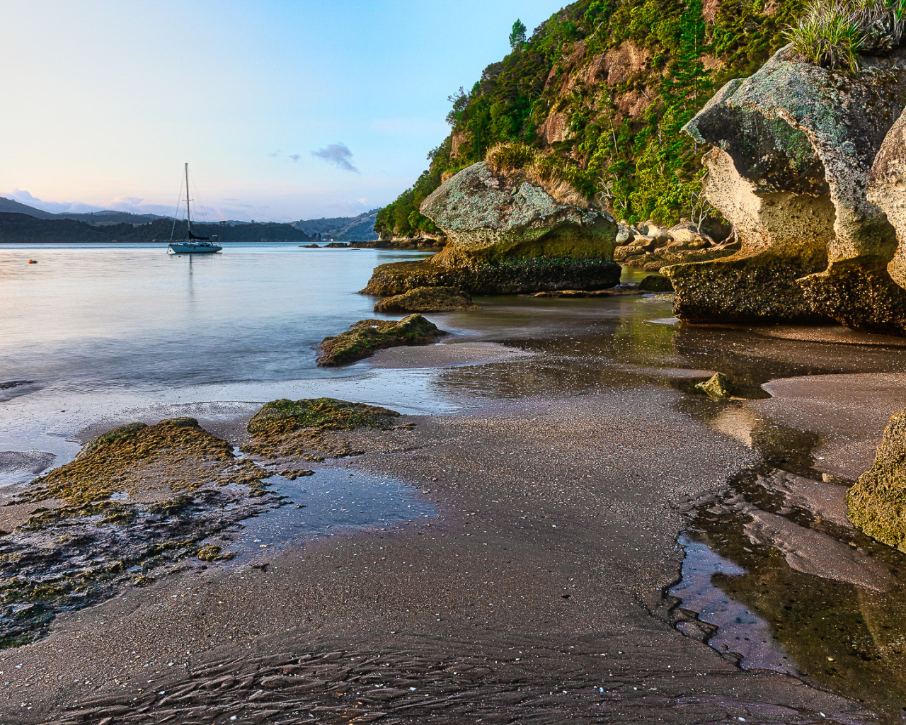 Мокрый песок и большие каменные глыбы на берегу залива