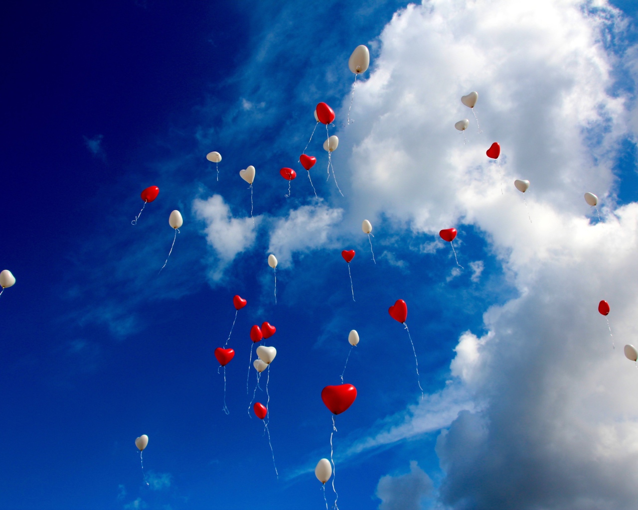 Many heart shaped balloons in the sky with white clouds