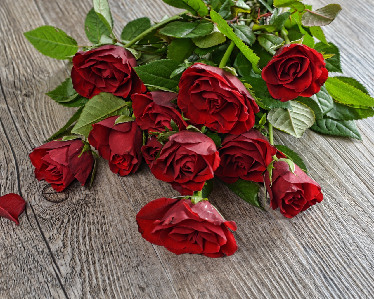 Красивый букет алых роз с зелеными листьями на деревянном столе