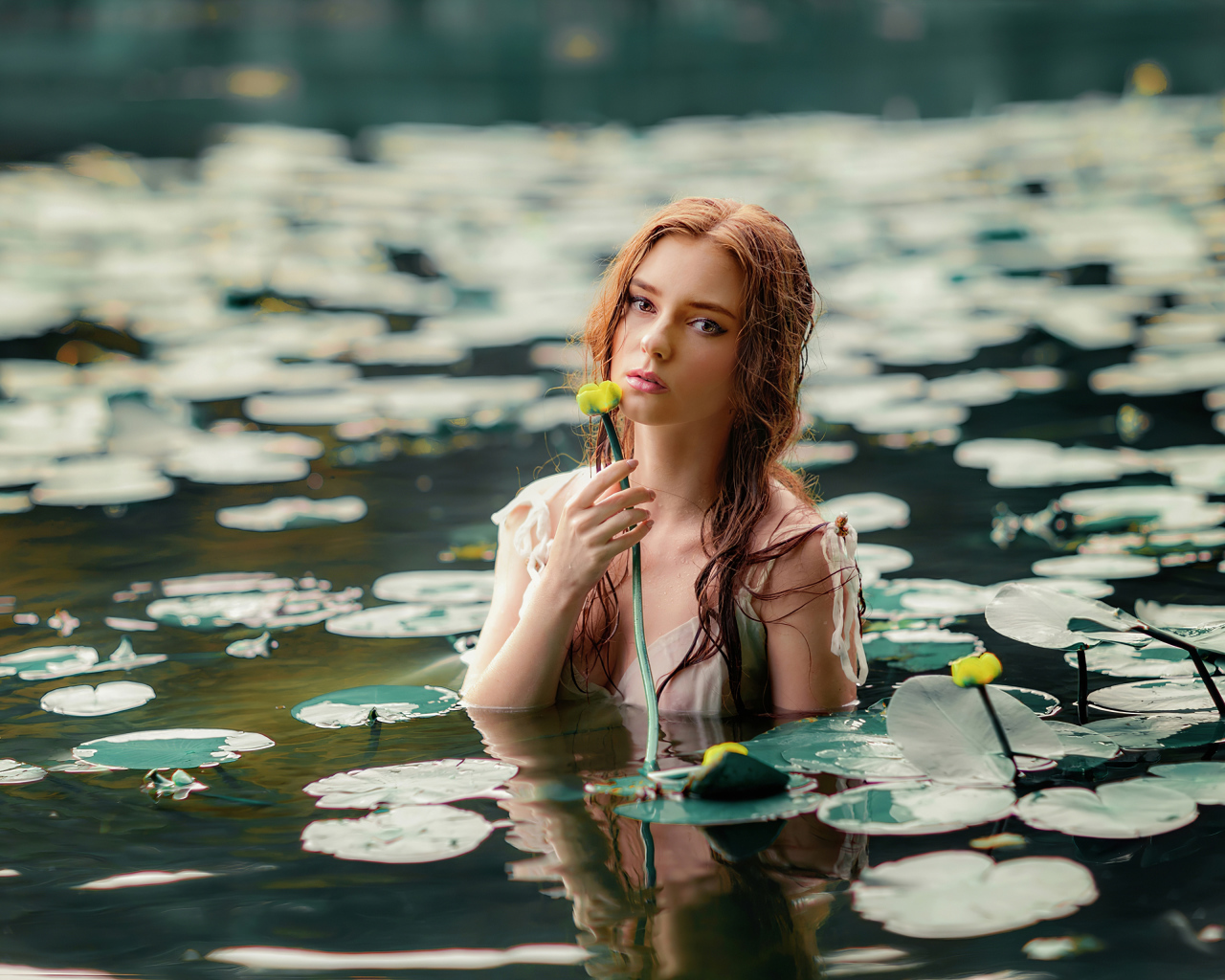 Красивая молодая девушка с водяными лилиями в пруду