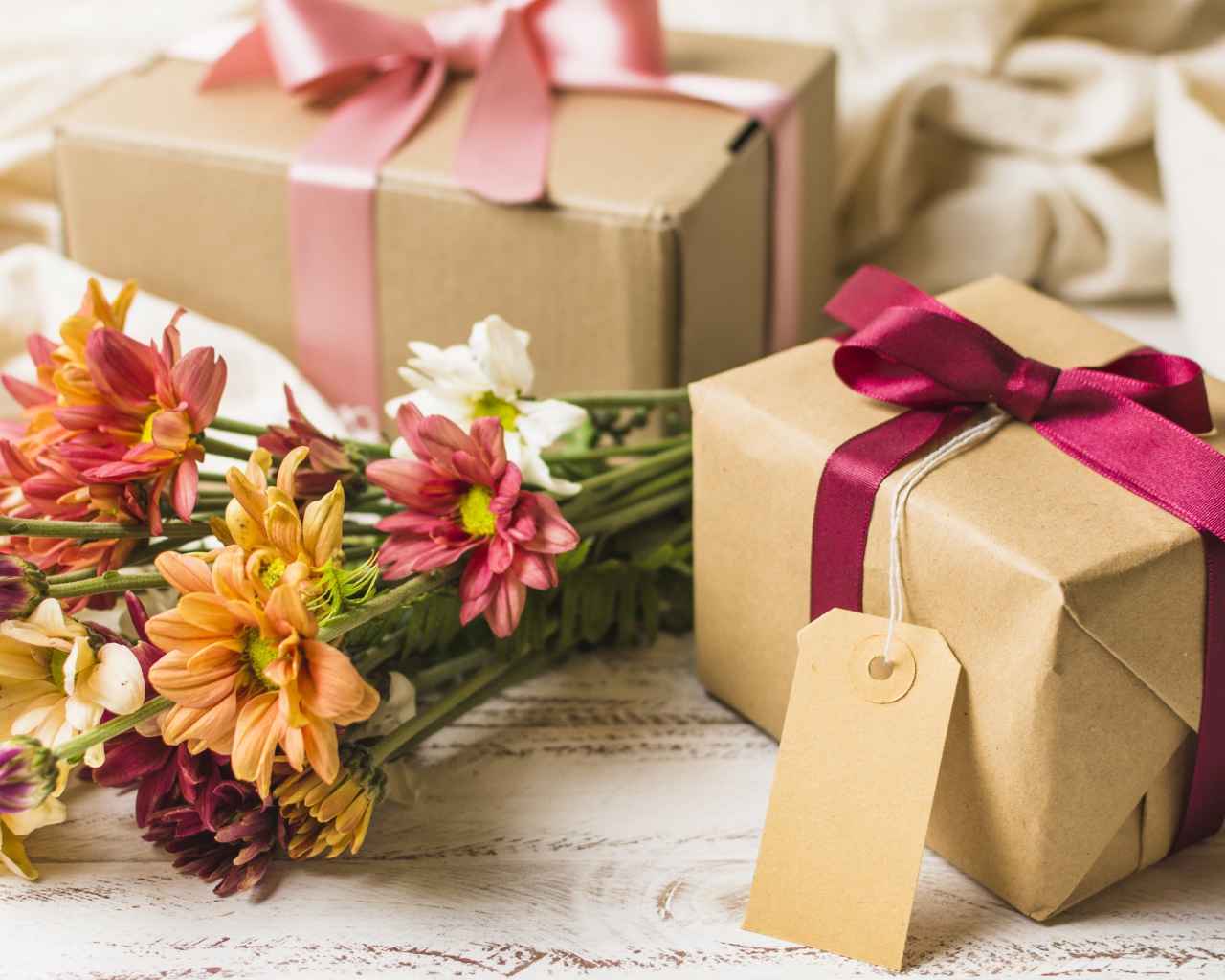 Букет разноцветных хризантем с подарками на столе 