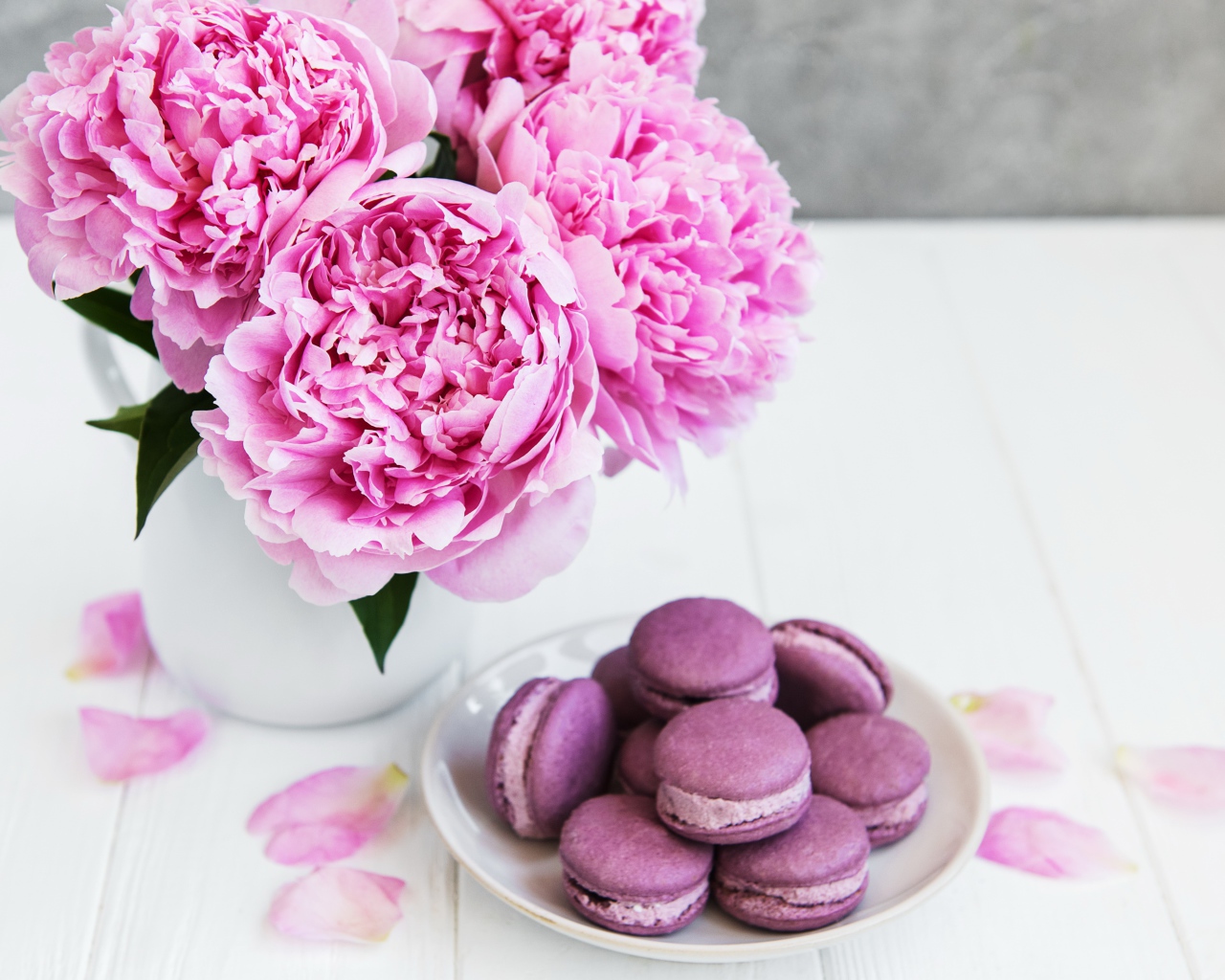 Букет розовых пионов на белом столе с десертом макарон 