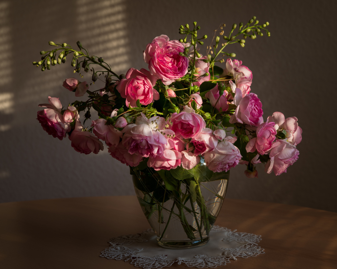 Букет розовых роз в стеклянной вазе не столе в лучах солнца 