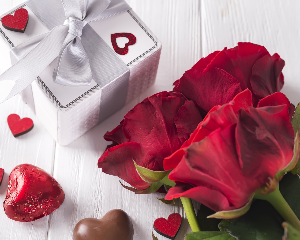 Букет красных роз на столе с конфетами и подарком